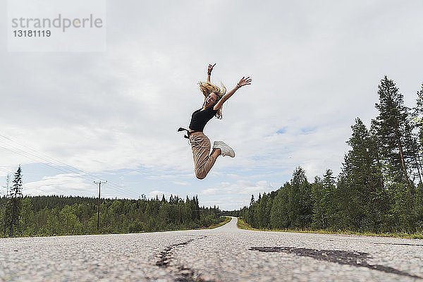 Finnland  Lappland  ausgelassene junge Frau springt in ländlicher Landschaft