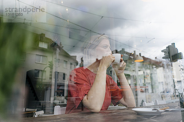 Junge Frau mit einer Tasse Kaffee hinter einer Fensterscheibe in einem Cafe