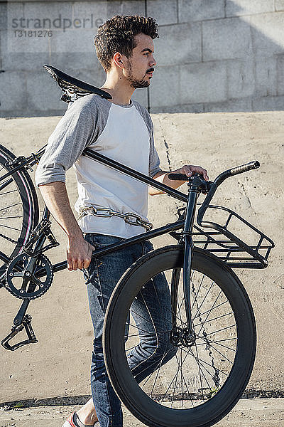 Junger Mann trägt Pendler-Fixie-Fahrrad an Betonmauer