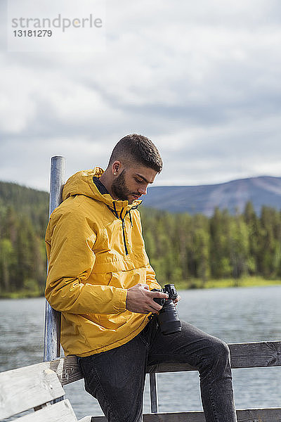 Finnland  Lappland  junger Mann mit einer Kamera auf einem Steg an einem See
