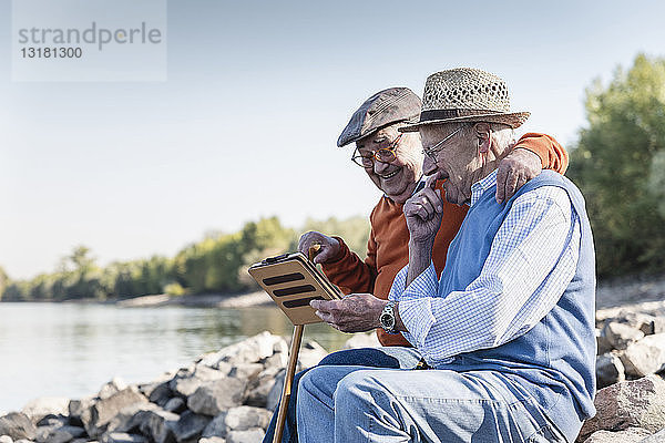 Zwei alte Freunde sitzen am Flussufer und benutzen ein digitales Tablett