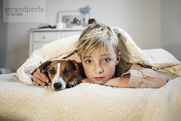 Porträt eines blonden Jungen und seines Jack-Russell-Terriers  die zusammen auf dem Bett liegen