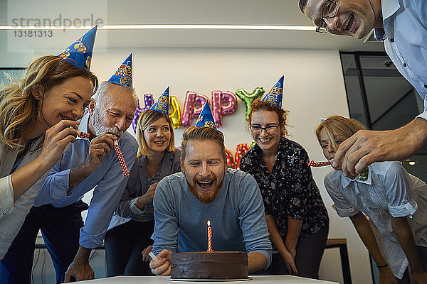 Kollegen mit einer Geburtstagsfeier im Büro mit Kuchen  Partyblower und Partyhüten