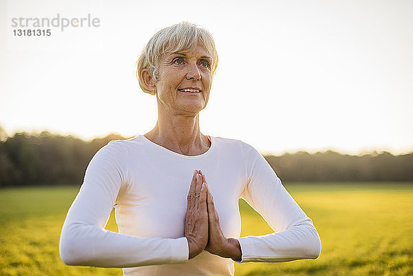 Ältere Frau macht Yoga auf einer ländlichen Wiese bei Sonnenuntergang