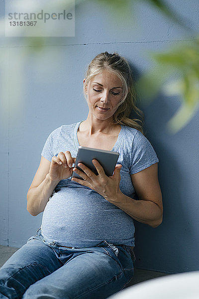 Schwangere Frau sitzt mit Tablette auf dem Boden
