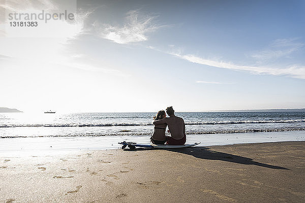 Frankreich  Bretagne  Rückansicht eines jungen Paares  das auf einem Surfbrett am Strand sitzt