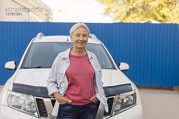 Porträt einer lächelnden älteren Frau  die vor ihrem Auto steht