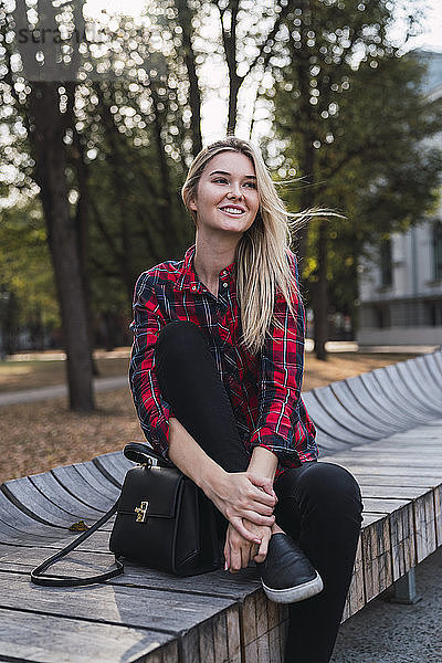 Porträt einer modischen jungen Frau mit Handtasche auf einer Bank im Freien sitzend