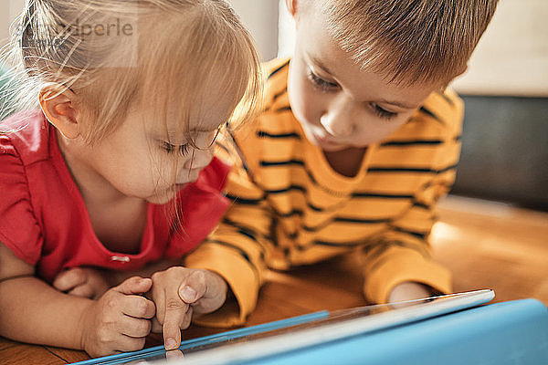Bruder und kleine Schwester liegen zu Hause auf dem Boden und benutzen ein digitales Tablett