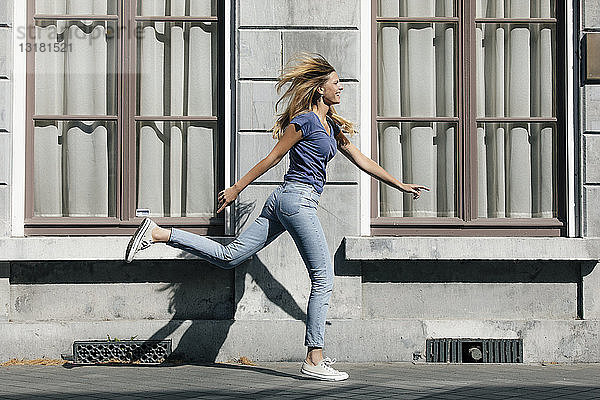 Niederlande  Maastricht  glückliche blonde junge Frau rennt an einem Gebäude in der Stadt entlang