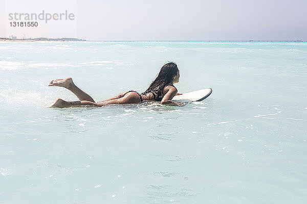 Junge Frau liegt auf einem Surfbrett  schwimmt auf dem Meer