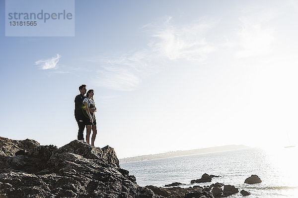 Frankreich  Bretagne  junges Paar steht bei Sonnenuntergang auf einem Felsen am Strand