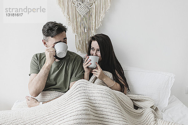 Glückliches Paar sitzt im Bett  trinkt Kaffee  hat Spaß
