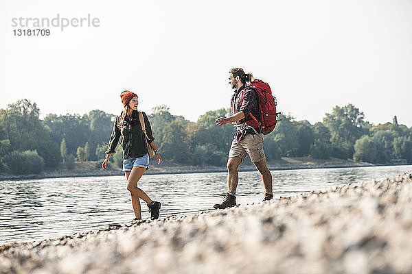 Junges Paar mit Rucksäcken beim Spaziergang am Flussufer