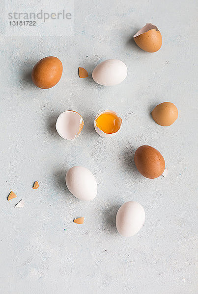 Ganze und geöffnete weiße und braune Eier auf hellem Boden