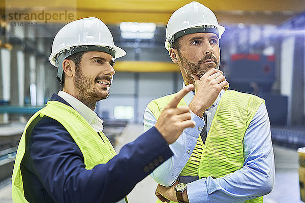 Zwei Manager in Arbeitsschutzkleidung im Gespräch in der Fabrik