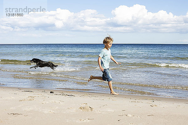 Junge mit Hund rennt am Strand
