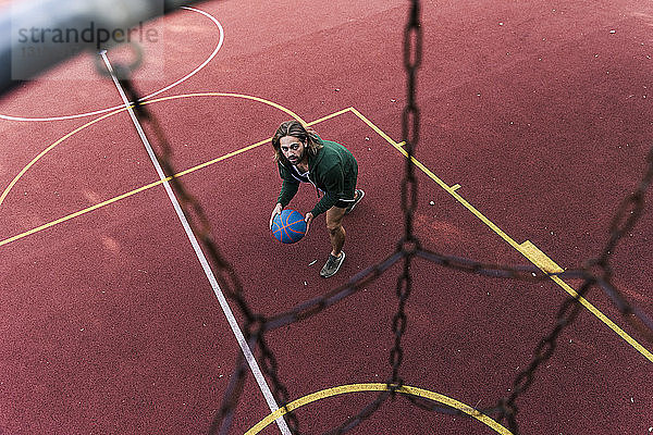 Junger Mann spielt Basketball auf Basketballplatz