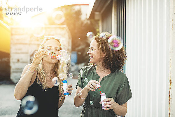 Zwei glückliche Frauen blasen Seifenblasen im Freien