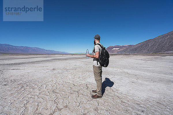 USA  Kalifornien  Death Valley  Mann mit Rucksack und Wasserflasche steht in der Wüste und schaut in die Ferne
