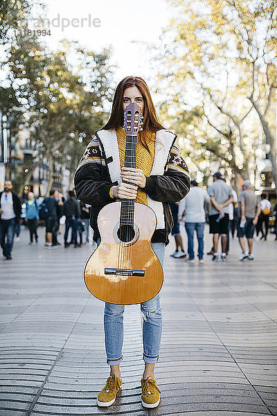 Rothaarige Frau mit Gitarre in der Hand in der Stadt