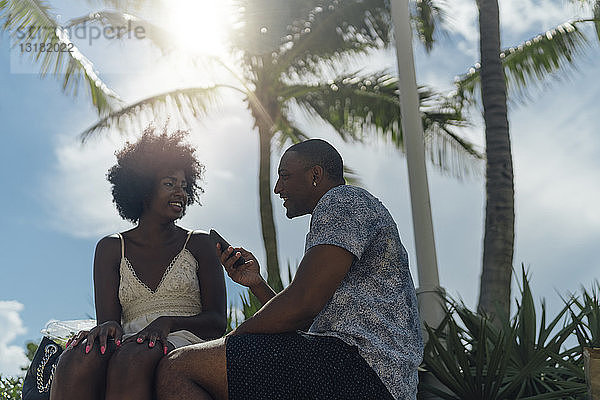 USA  Florida  Miami Beach  lächelndes junges Paar mit Handy im Park beim Telefonieren