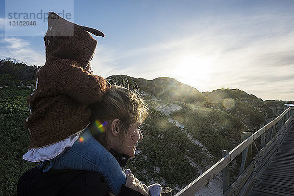 Mutter und kleines Mädchen  auf den Schultern sitzend  auf dem Weg zum Strand von Boulders