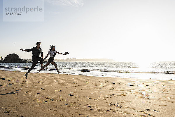 Frankreich  Bretagne  glückliches junges Paar springt bei Sonnenuntergang an den Strand