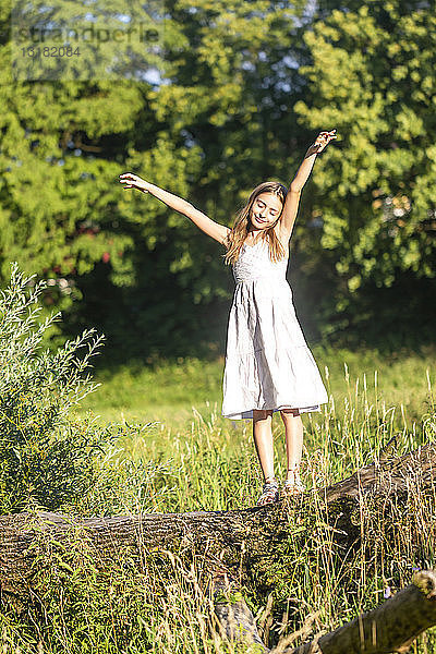 Porträt eines lächelnden Mädchens  das auf einem Baumstamm steht und sich am Sonnenlicht erfreut