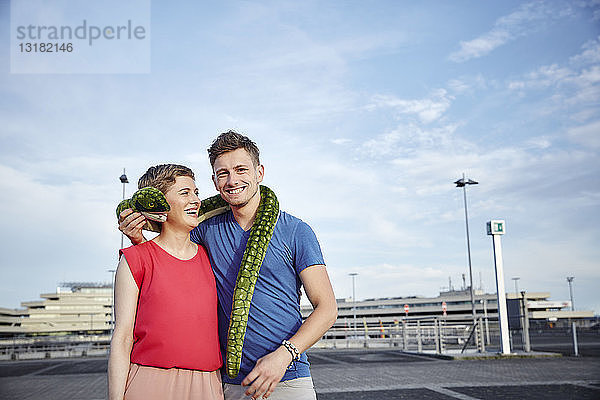 Porträt eines glücklichen Paares mit Plüschschlange vor dem Flughafen