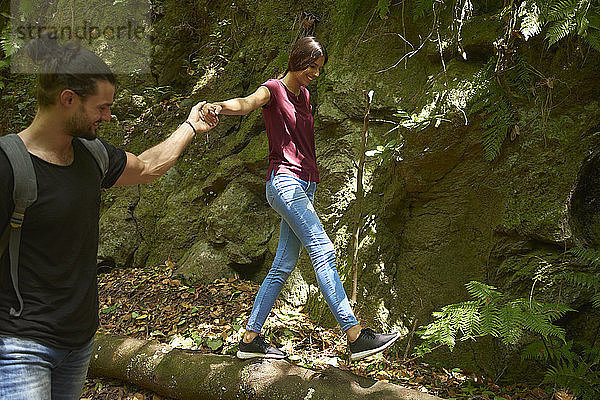 Spanien  Kanarische Inseln  La Palma  lächelnder Mann hält Hand der Freundin  die auf einem Baumstamm balanciert