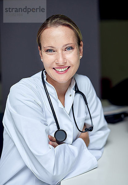 Porträt einer lächelnden Ärztin mit Stethoskop am Schreibtisch sitzend