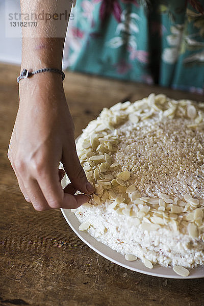 Frauenhand garniert selbstgebackenen Kuchen mit Mandelsplittern  Nahaufnahme