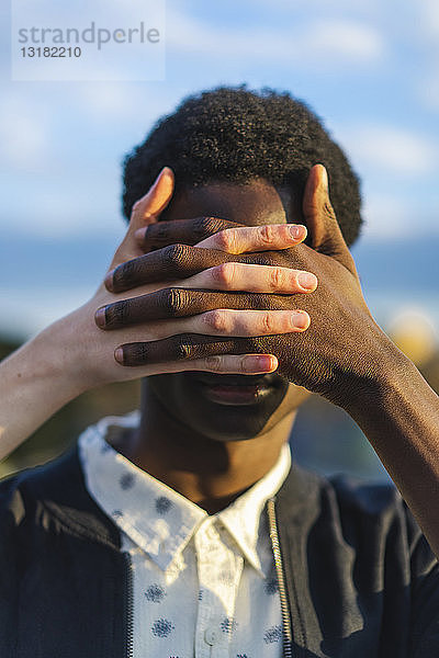 Hände bedecken die Augen eines jungen schwarzen Mannes