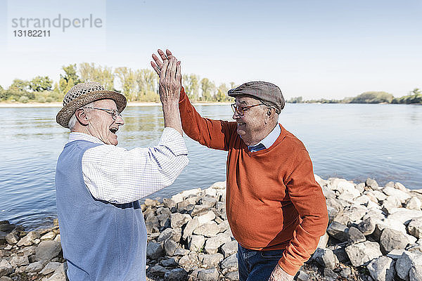 Zwei lachende alte Freunde beim Abklatschen an einem See