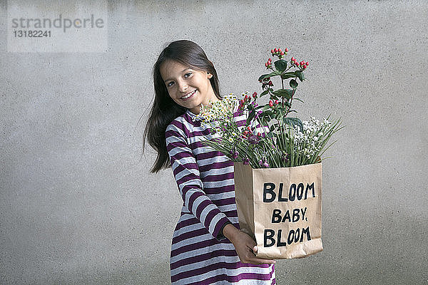 Porträt eines glücklichen Mädchens  das eine Papiertüte mit Blumen hält