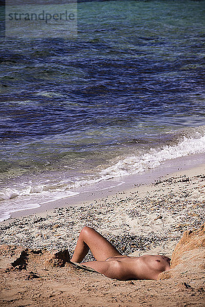 Nackte Frau beim Sonnenbaden am Strand am Meer