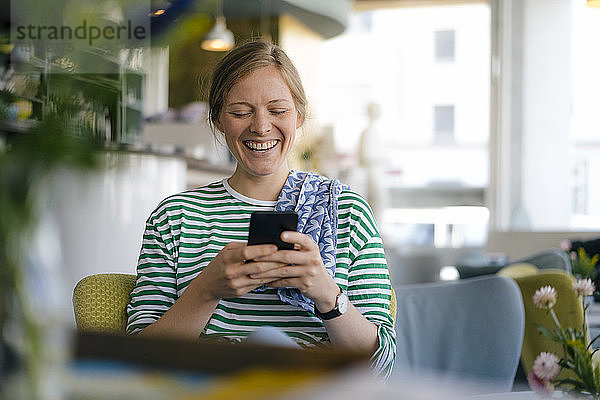 Lachende junge Frau  die in einem Cafe mit dem Handy telefoniert