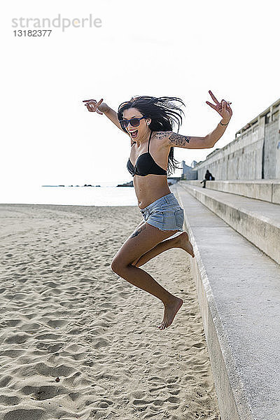 Porträt einer glücklichen jungen Frau  die auf den Strand springt