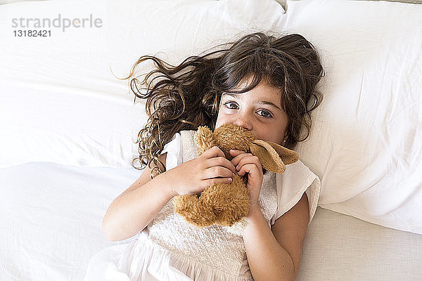 Kleines Mädchen liegt mit Plüschkaninchen im Bett