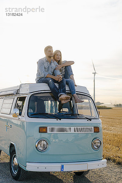 Liebenswertes junges Paar auf dem Dach eines Wohnmobils in ländlicher Landschaft