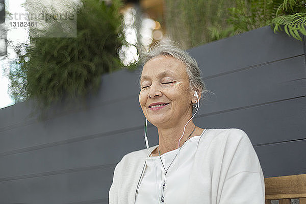 Lächelnde ältere Frau mit geschlossenen Augen  die im Freien Kopfhörer trägt
