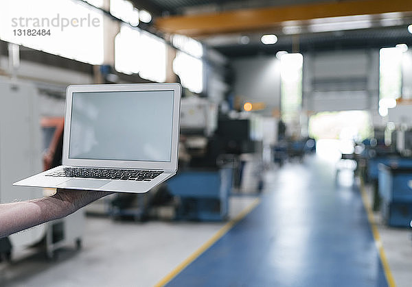 Handgehaltener Laptop mit leerem Bildschirm in einer Fabrikhalle