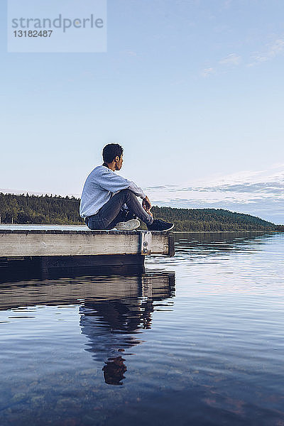 Junger Mann sitzt am Inari-See und schaut auf Aussicht  Finnland