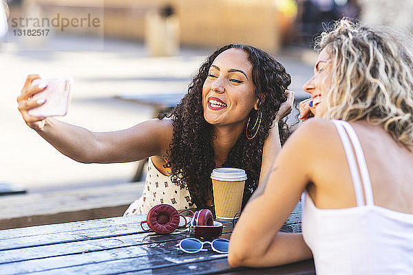 Zwei glückliche Freunde  die sich bei Tisch im Freien ein Selfie gönnen