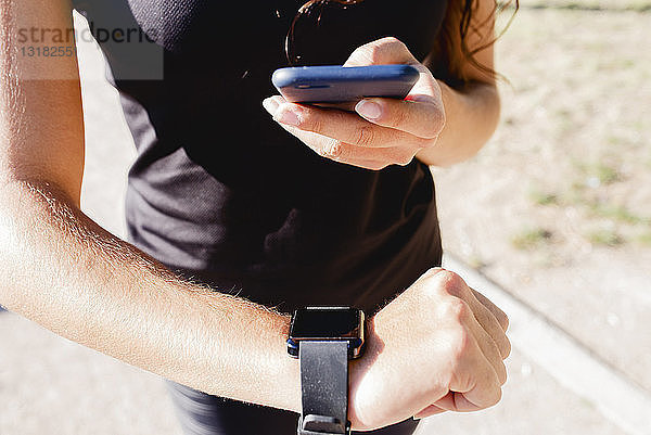 Nahaufnahme einer sportlichen jungen Frau mit Handy und Smartwatch