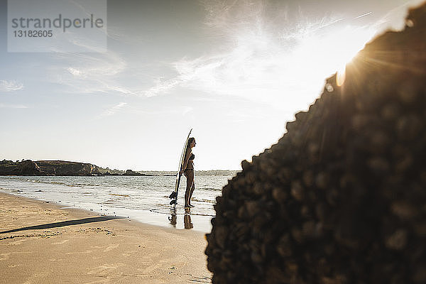 Frankreich  Bretagne  junge Frau mit Surfbrett am Meer stehend