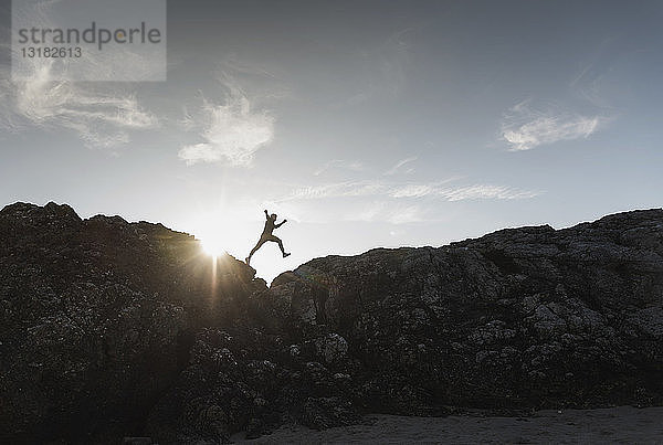 Frankreich  Bretagne  junger Mann springt bei Sonnenuntergang auf einen Felsen