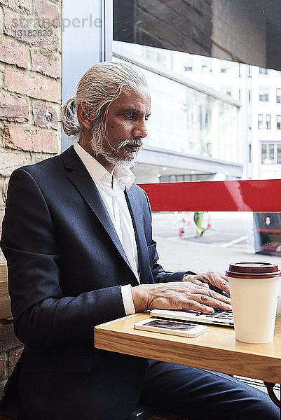 Leitender Geschäftsmann sitzt in einem Café und arbeitet am Laptop