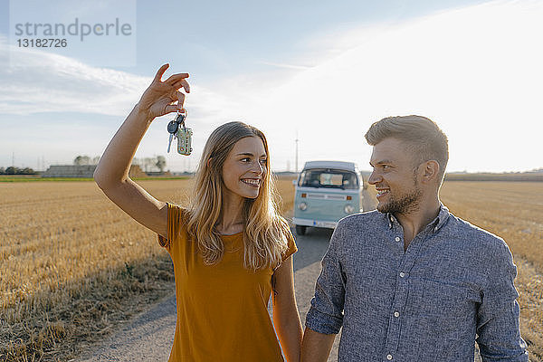 Junges Paar mit Autoschlüssel auf Feldweg am Wohnmobil in ländlicher Landschaft